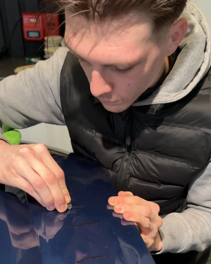 Alex carefully working on the paintwork of a blue vehicle.