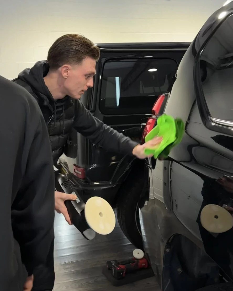 Alex wiping a black vehicle with a microfibre cloth, with a polishing machine in hand.